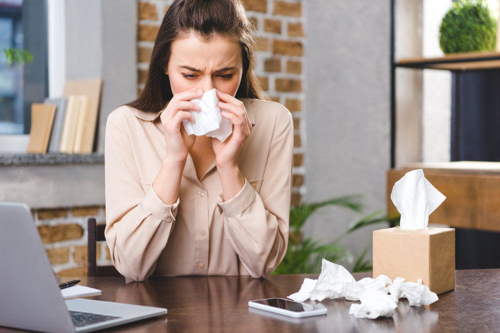 Woman sitting at desk and blowing her nose.