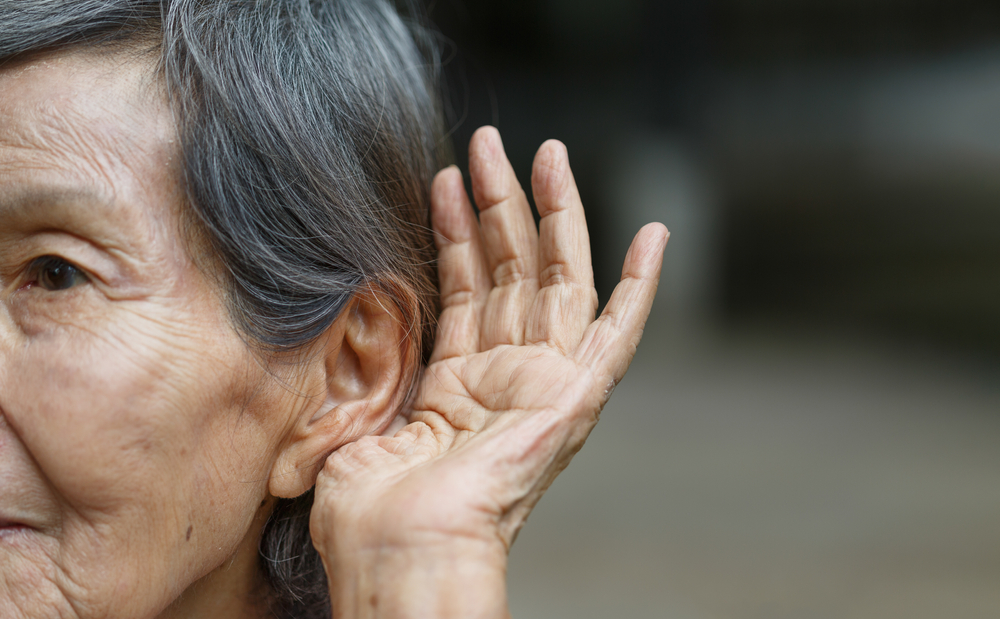 Older woman holding hand up to her ear to try and hear